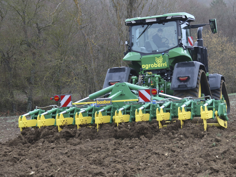 Subsolador baabor modelo SF530 plegable trabajando en un campo con la tierra húmeda, con un tractor John Deere 8RX